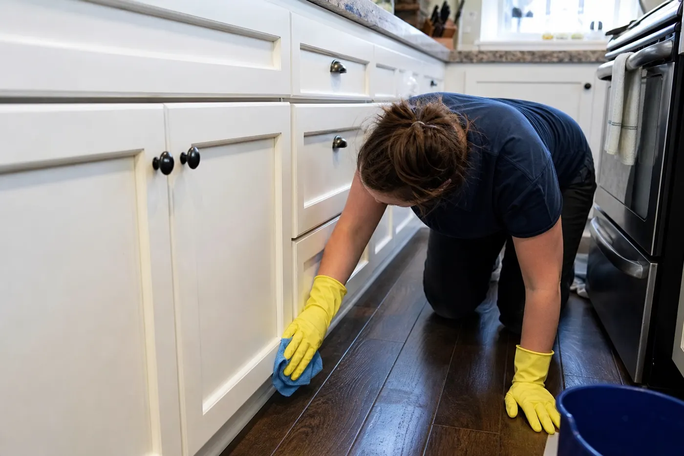 Cleaner wiping baseboards and cabinet fronts on a deep clean